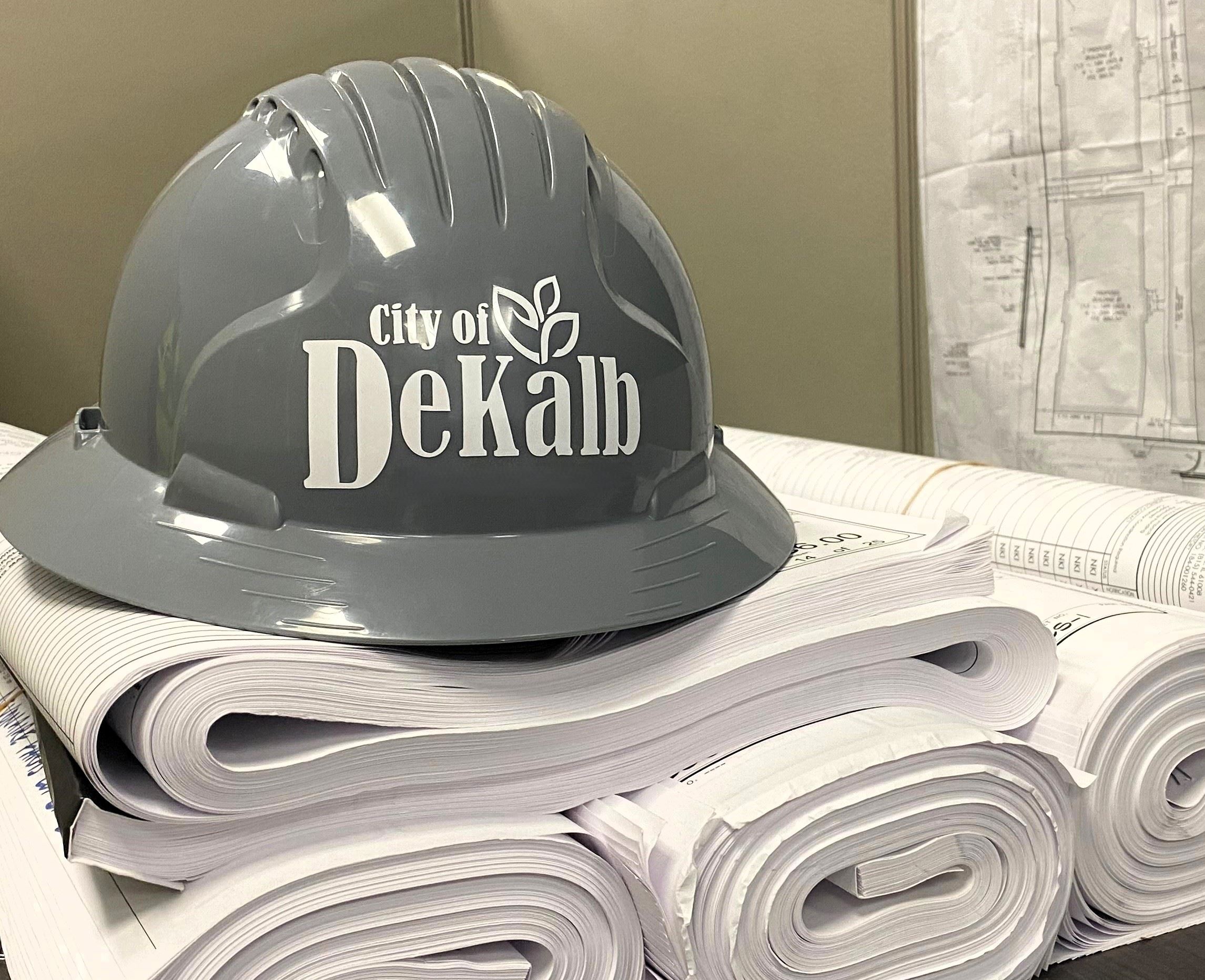 A gray hard hat with the City's logo on top of a pile of building plans
