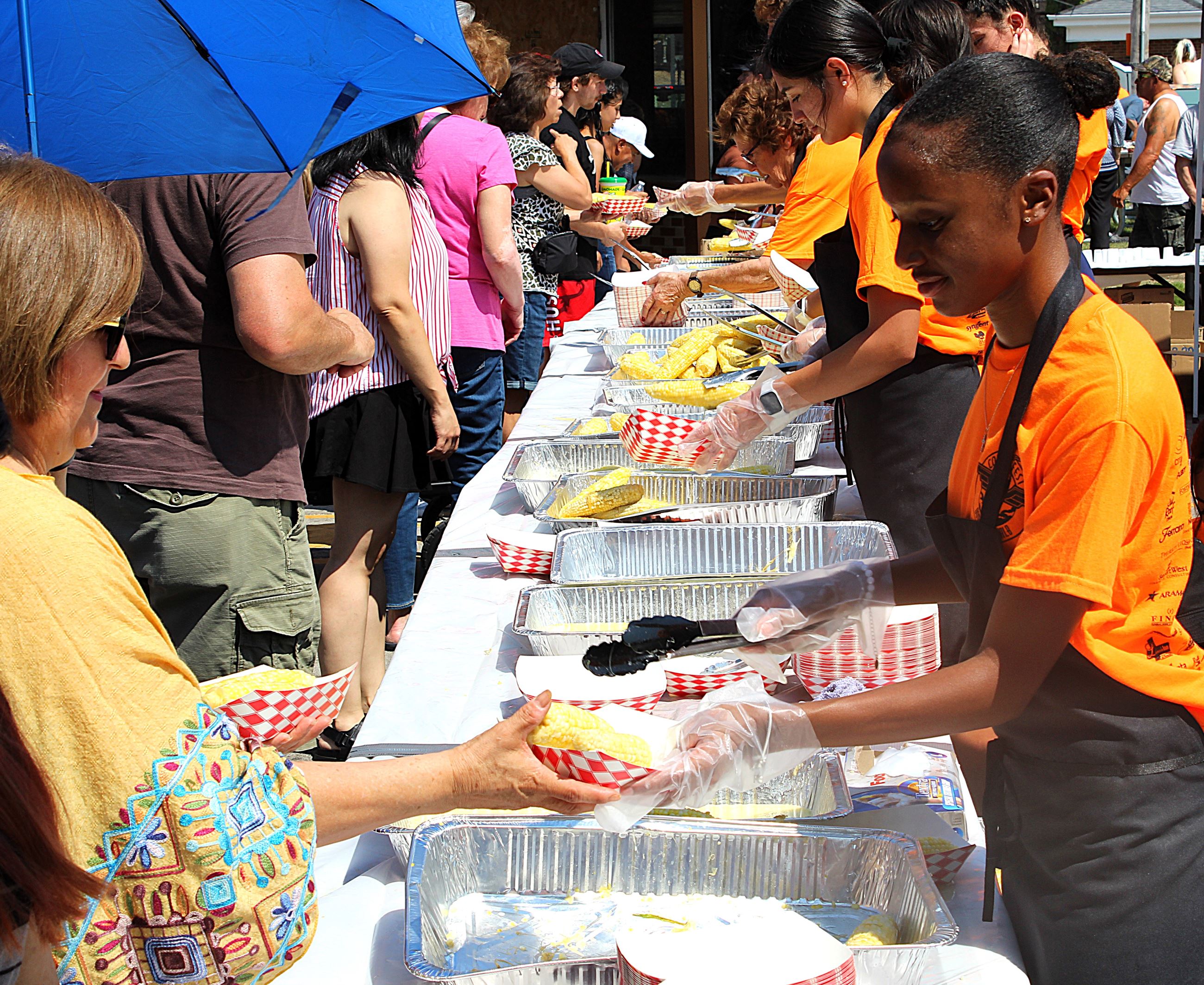 A woman hands another woman corn on the cob during the corn boil.